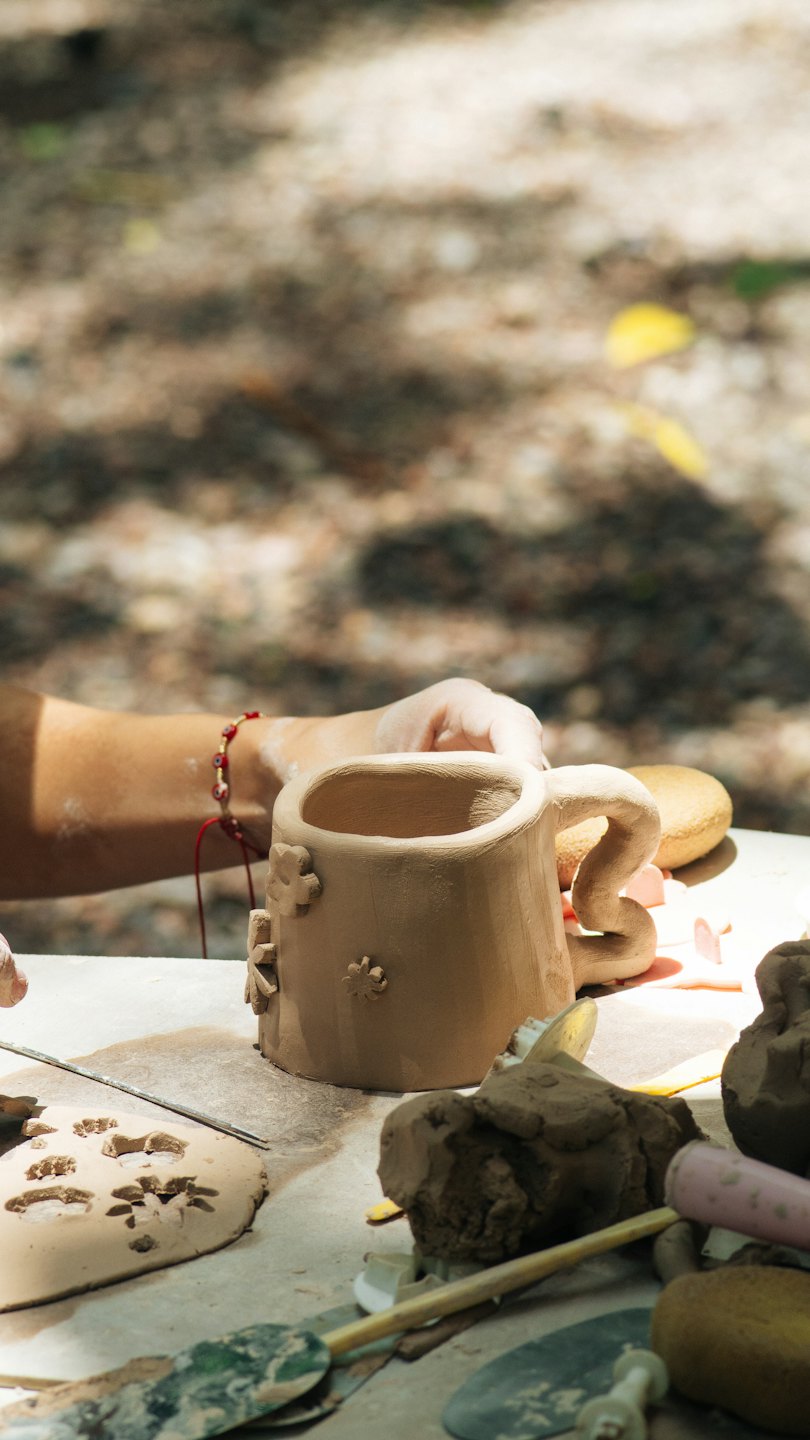 Hands shaping a clay mug with flower details on a workbench.